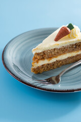 Carrot cake slice with cream cheese frosting on blue background