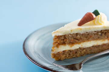 Carrot cake slice with cream cheese frosting on blue background