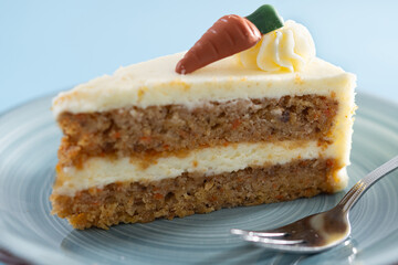 Carrot cake slice with cream cheese frosting on blue background