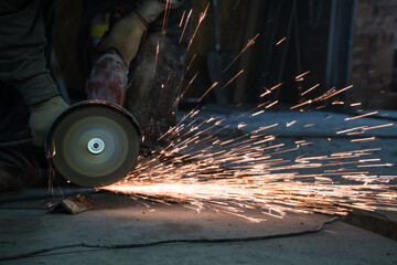 The sides fly bright sparks from the angle grinder machine. A male in a working gloves grinds a metal product with angle grinder. Cutting metal causing sparks isolated - a series of METAL INDUSTRY.