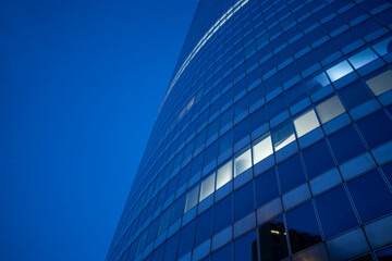 Curved glass skyscraper facade with blue sky reflection showing modern corporate architecture and sleek urban design rising upward