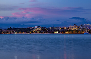 Fototapeta premium Twilight panoramic view of Side coast with illuminated hotels and resorts. Purple sunset clouds over the Mediterranean sea and Taurus mountains in the background. October, Antalya region, Turkey.