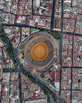 Aerial view of the iconic Plaza de Toros de la Maestranza stands as a terracotta jewel amidst the dense urban tapestry, Seville, Andalusia, Spain.
