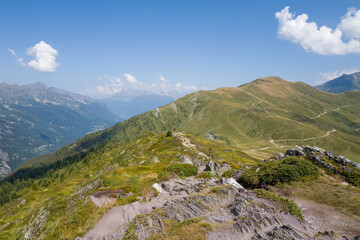 Obraz premium Rocky mountain ridge overlooks rolling green slopes crisscrossed by winding paths under a clear blue sky in the Aiguillettes des Posettes region.