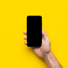 Hand holding a smartphone with blank screen on yellow background