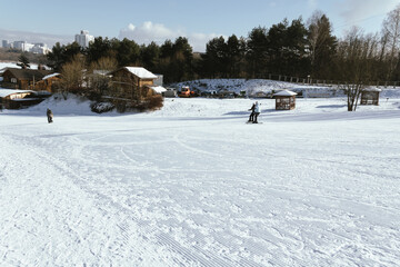 People skiing on a wide slope overlooking a mountain village. Active recreation on a ski slope, resort during holidays, weekend on a ski slope, resort with a modern chalet.