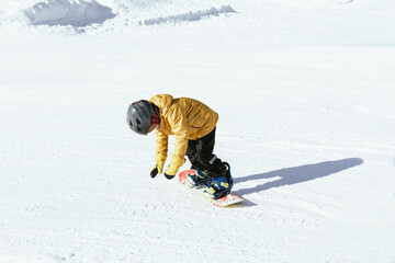 Cute little boy on snowboard, wearing yellow jacket, riding snowboard on ski slope, resort during holidays, weekend.