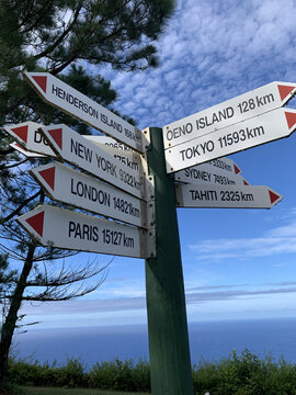 View of a signpost pointing to distant cities like New York, London, and Paris, against the backdrop of the sea, Adamstown, British Overseas Territory in the Pacific Ocean.