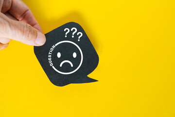 hand hold real black speech bubble paper cut with bad emotion face icon and question mark on blue background