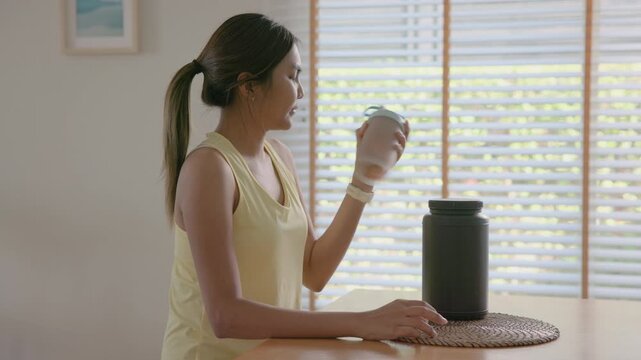 Young adult gen z active woman drink whey protein shake boost bottle diet food gain build muscle after home workout. health care black asia people happy relax sport protect aging life weight loss.