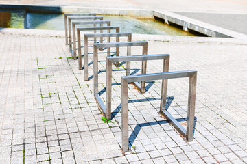Modern metal bicycle racks stand empty on paved ground. Sleek, square U-shaped design awaits cyclists in the sunny public space