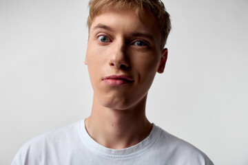 Fototapeta premium Young man in a studio with neutral background, close up of the face and calm expression, white shirt, clean lighting, focusing on mood, features and subtle details of skin tone