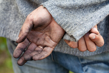 Dirty, overworked male hands. A man dressed in a sweater and jeans holds dirty hands behind his back.