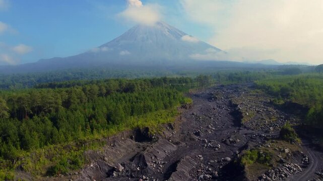 Stone river, stone deposit and Mount Semeru. Volcano clouds of smoke against the blue sky. Active volcano on the island of Java in Indonesia. Ash pillar from a bird's eye view. Dron. 4K