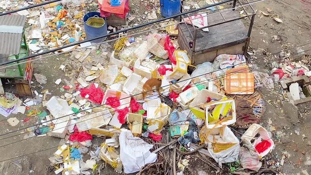 garbage and plastic debris beside slum buildings, highlighting urban pollution and sanitation problems in Bangladesh.