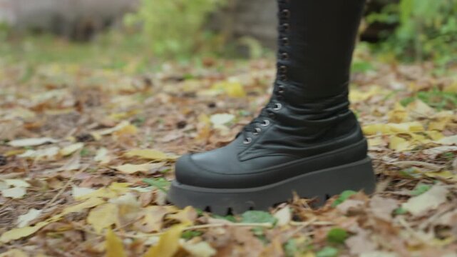 black leather boots walking on leaves, laced combat boots stepping over log pile, crunchy autumn underfoot, mossy bark and scattered timber, lowangle cinematic close frame with edgy rock fashion vibe