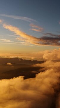 Vertical aerial view of golden clouds and mist over dark mountain ridges during sunset or sunrise