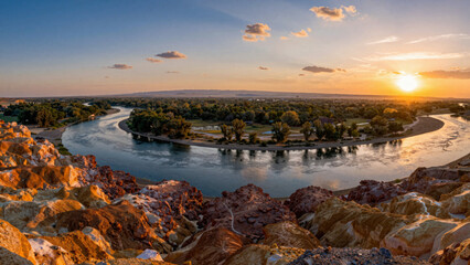 Fototapeta premium Majestic winding river meanders through a vibrant geological landscape, illuminated by a breathtaking golden sunset over a serene natural valley