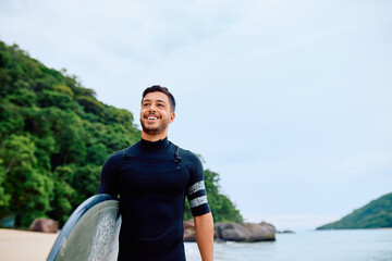 Young man surfer holding surfboard walking on a tropical beach, smiling and having fun. Lifestyle, summer, vacation concept