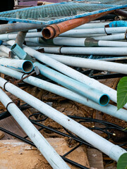 Stack of Used White and Blue PVC Pipes with Rusty Metal Pipes