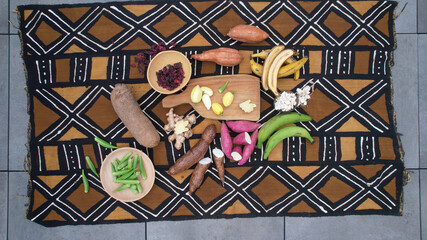 Assortment of West African root vegetables and fruits arranged on a traditional mud cloth © august.columbo