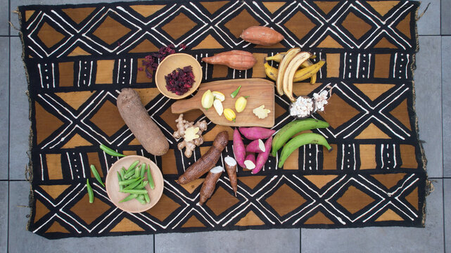 Assortment of West African root vegetables and fruits arranged on a traditional mud cloth