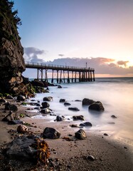 Fototapeta premium Pier extending into ocean, next to rock face, serene light, and blurred water motion captured in the golden hour