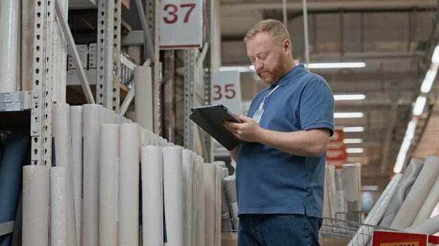 Experienced home improvement shop employee using black tablet to review assortment during workday