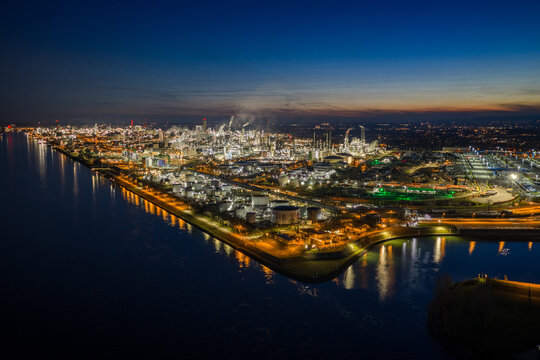 Aerial view of sprawling BASF industrial complex with illuminated structures casting reflections on the dark waters below, Ludwigshafen am Rhein, Rheinland-Pfalz, Germany.