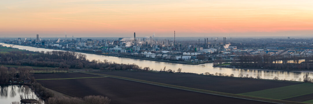 Aerial view of the river reflecting the pastel sky, flowing past the industrial BASF complex with its stark contrasts against the fields, Ludwigshafen am Rhein, Rheinland-Pfalz, Germany.