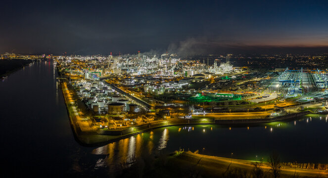 Aerial view of the sprawling BASF industrial complex ablaze with lights reflecting on the dark waters, Ludwigshafen am Rhein, Rheinland-Pfalz, Germany.