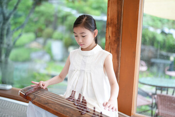 A young girl is playing a traditional Chinese instrument, the guzheng, in a room with a view of a...
