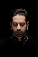 Fototapeta premium A DJ stands with eyes closed, wearing headphones. The background is dark. He appears to be concentrating on the music as his head is slightly bowed. This moment captures a deep connection to sound.