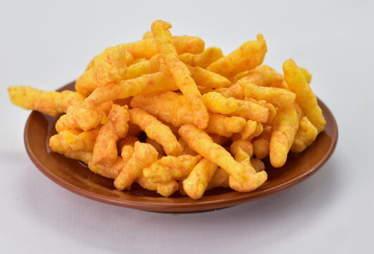 Crunchy cheese flavored corn puff sticks on a ceramic plate.