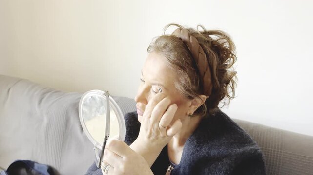 charismatic mature lady in her 50s or 60s performing daily hygiene by shaping her brows with a cosmetic tool, initially looking serious and focused on the reflection. confidence, and finding joy 