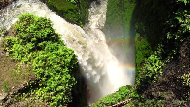 Blawan Waterfall in the Kawa-Ijen crater area, hidden in the tropical jungle, East Java, Indonesia. View of a powerful waterfall and a colorful rainbow surrounded by lush greenery. Dron. 4K