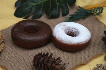 Two donuts, one chocolate glazed and one powdered sugar, styled on burlap cloth with decorative...