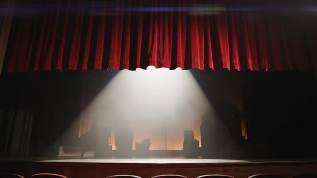 Red velvet theater curtains opening on a spotlight casting a light on the stage and set design