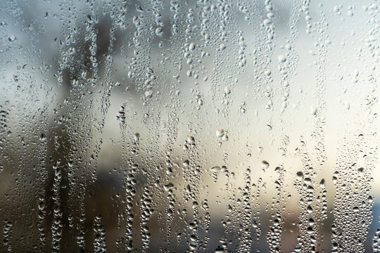Raindrops and condensation on window glass with blurred outdoor background. Close-up texture photography. Rainy weather and moisture concept for design, banner, poster, wallpaper. Macro shot with copy