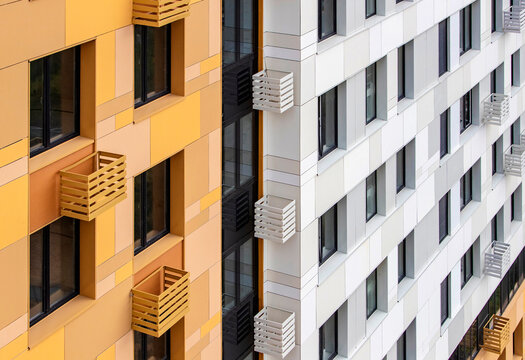 Two buildings with different colors and balcony designs sit next to each other in an urban area. The scene shows the contrast in architecture and building style.