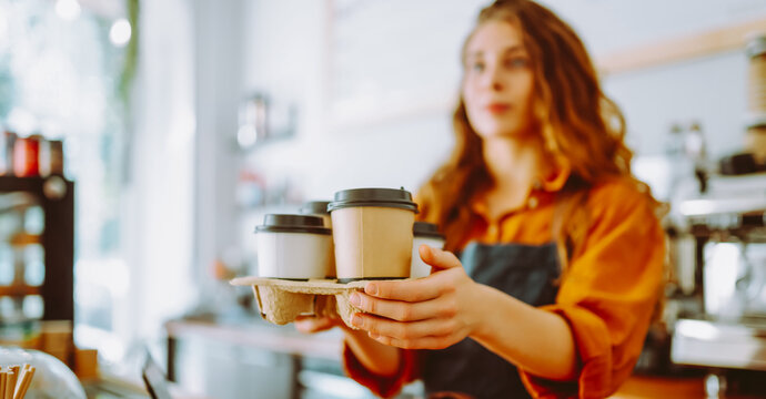 A portrait of a young woman stands in a coffee shop with a digital tablet at the bar on a sunny day. A female barista works in a cozy coffee shop. Small business concept, beverages, and technology. - Powered by Adobe