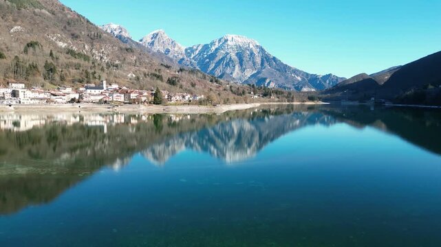 Aerial drone footage of Barcis Lake, Italy: sunny winter day, turquoise water and mountains, with snow-capped peaks visible in the distance. Ideal for travel, nature and scenic stock footage.