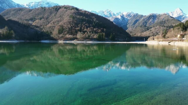 Aerial drone footage of Barcis Lake, Italy: sunny winter day, turquoise water and mountains, with snow-capped peaks visible in the distance. Ideal for travel, nature and scenic stock footage.