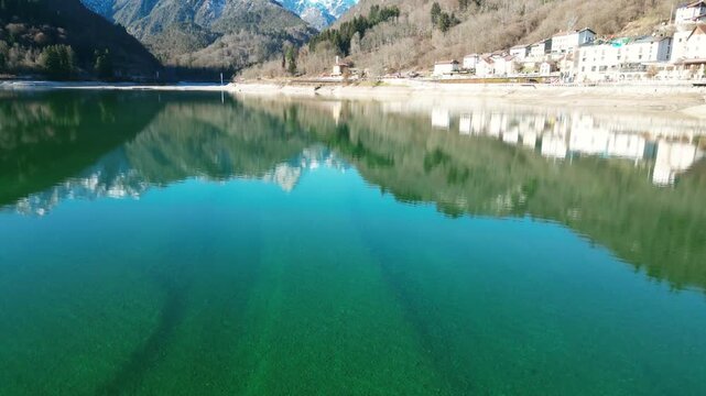 Aerial drone footage of Barcis Lake, Italy: sunny winter day, turquoise water and mountains, with snow-capped peaks visible in the distance. Ideal for travel, nature and scenic stock footage.