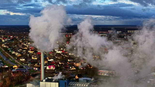 Aerial view of industrial plant with white smoke emitting from tall chimneys over Jelgava city skyline on winter day in Latvia