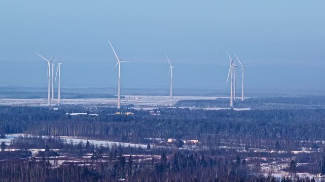 Drone shot of wind farm with still turbines standing in frozen field and pine forest on calm windless day in winter Latvia