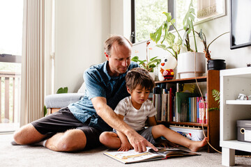 Boy reading book with dad at home on the floor