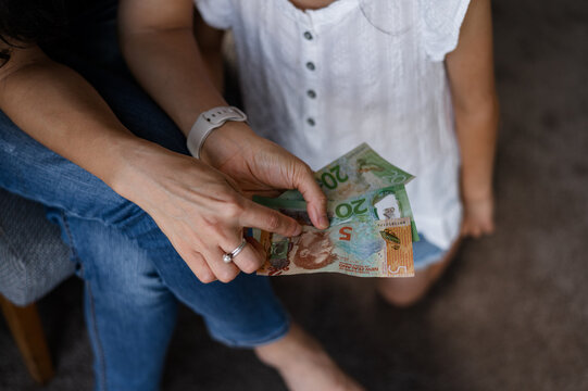 A young child examines New Zealand banknotes while seated beside an adult