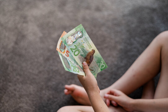 Young child relaxes on the carpet, holding several New Zealand banknotes in one hand