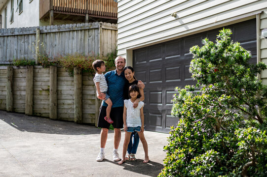 A family of four poses happily outdoors, celebrating a sunny day in their driveway